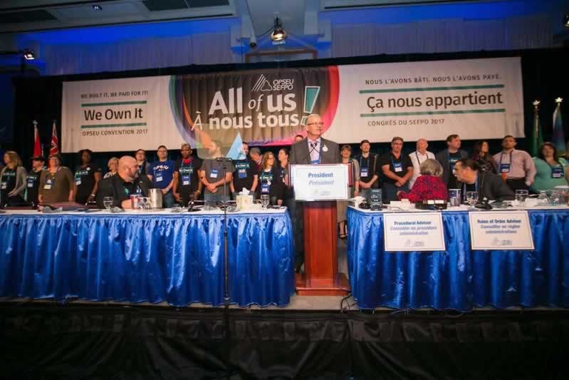 OPSEU President Warren (Smokey) Thomas introducing the We Own It mobilizers standing behind him onstage during Convention 2017 Day 1