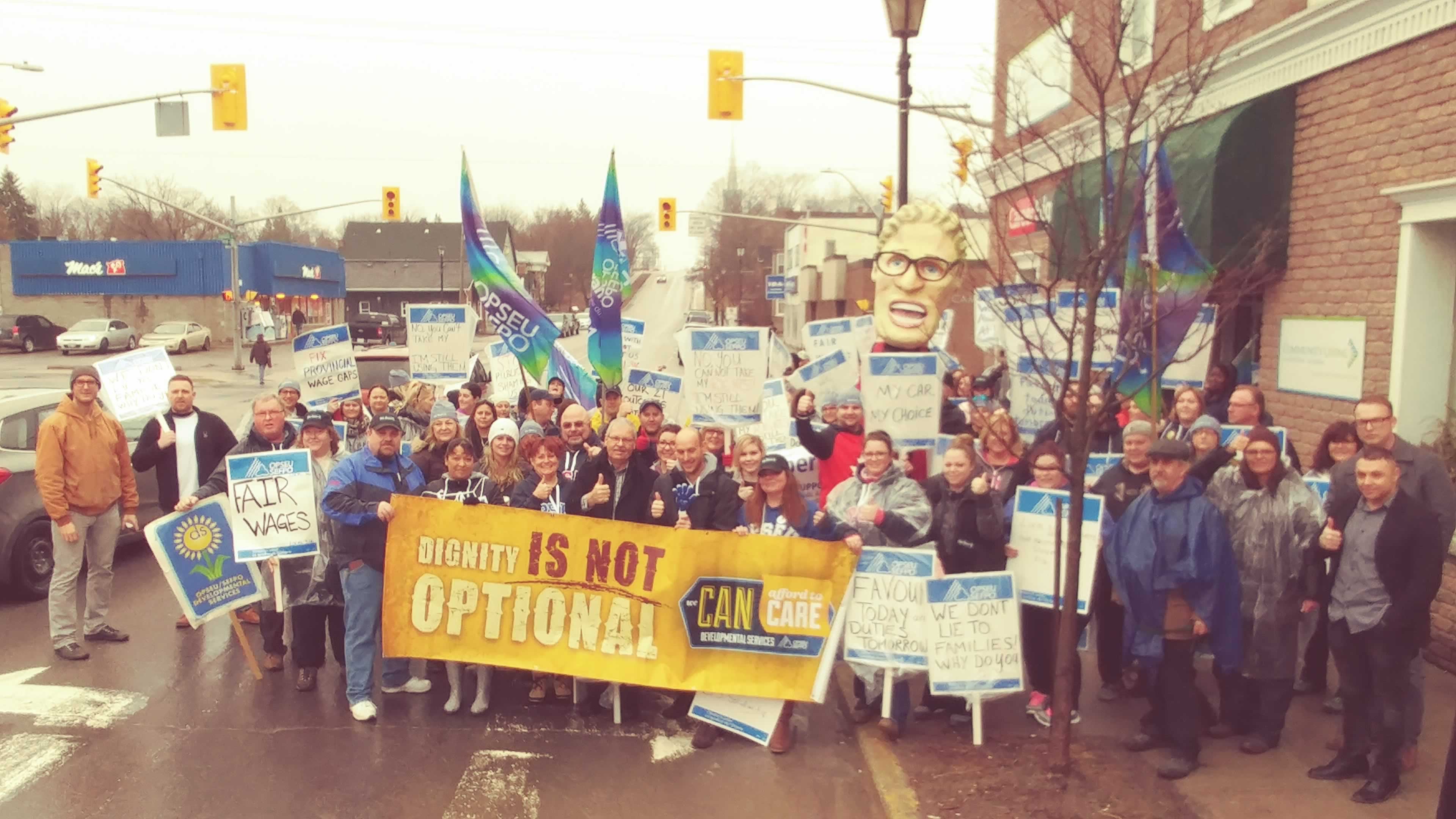 Large group of OPSEU members holding picket signs, flags, and banners during a rally in Campbellford.