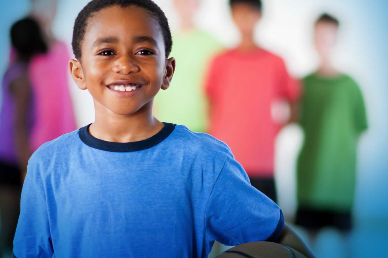 Young boy in a blue shirt smiles as (faded) children look on behind