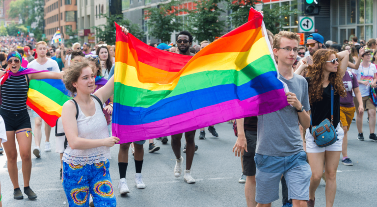 Two young people are holding a rainbow flag at a parade